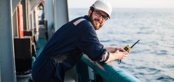 Deck Officer on deck of offshore vessel or ship , wearing PPE personal protective equipment. He holds VHF walkie-talkie radio in hands. Dream work at sea